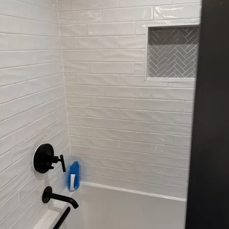 White tiled bathroom shower with black faucet fixtures and a blue shampoo bottle on the tub edge.