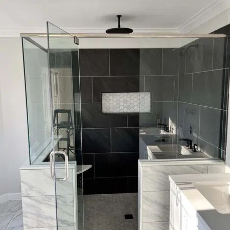 Modern walk-in shower with glass door, black tile walls, hexagonal niche, and marble tile accents in bathroom.