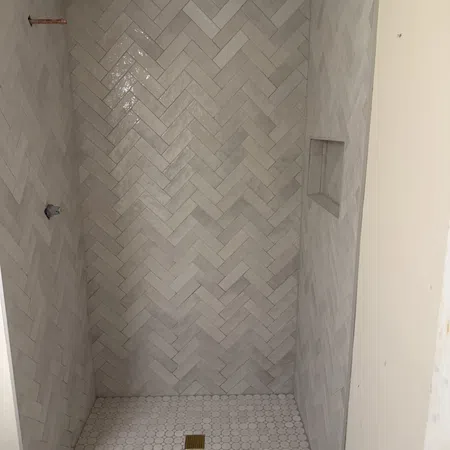 Shower with light grey herringbone wall tiles and round mosaic floor tiles with brass drain cover