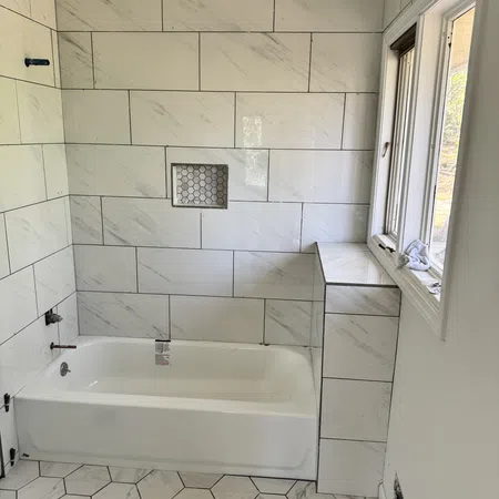 Modern bathroom with white marble wall tiles, hexagonal floor tiles, built-in bathtub, and window natural light.