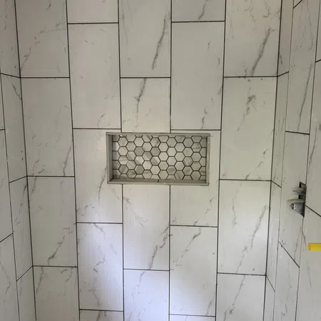 Shower area tiled with large white marble-effect rectangles and a recessed hexagon-tiled niche with white and gray tiles.