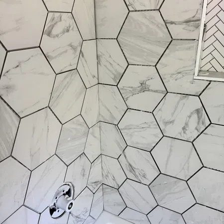 Hexagonal marble-patterned tiles covering bathroom walls around a bathtub with plumbing fixtures in progress.