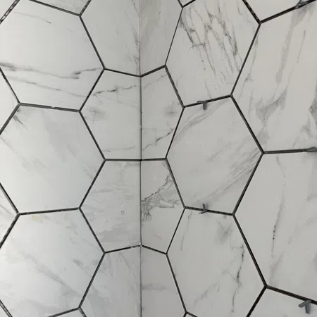Close-up of marble hexagonal tiles installed on a wall with spacers between grout lines.