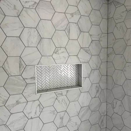 Bathroom wall with large hexagonal marble tiles and inset shelf with herringbone pattern tiles.