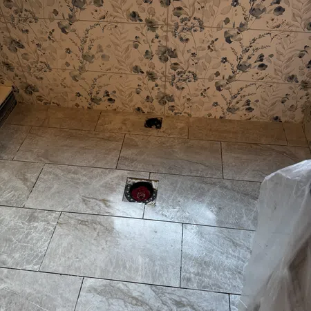 Gray marble floor tiles with a red drain hole in the center and floral patterned wall tiles in the background.