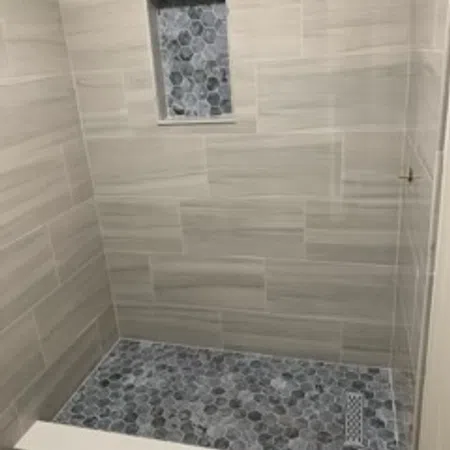 Shower with beige rectangular wall tiles and dark hexagonal mosaic floor tiles with matching niche