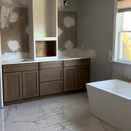 Modern bathroom under renovation with brown wooden cabinets, white freestanding tub, and glossy marble tile floor.
