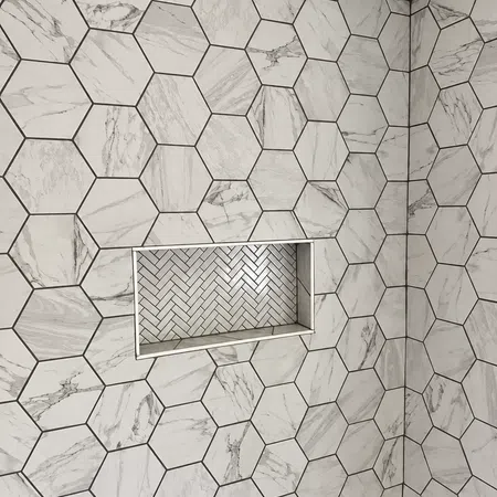 Shower wall with large hexagonal marble tiles and a recessed niche featuring white herringbone tiles.