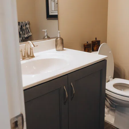 Small bathroom with white toilet, dark wood vanity, modern silver faucet, and beige walls.