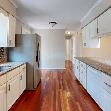 Bright kitchen with white cabinets, granite countertops, stainless steel fridge, and polished hardwood floors.