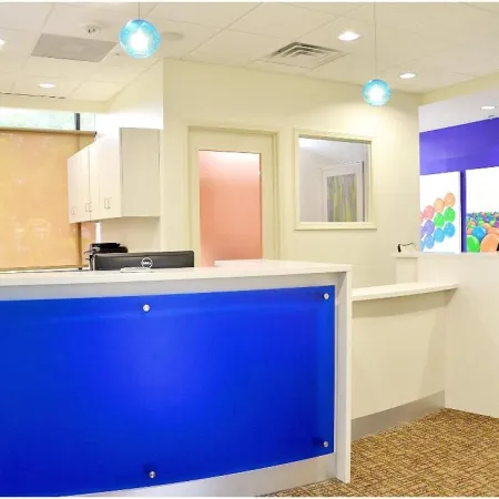 Modern reception area with blue and green front desks, colorful balloon artwork, and pendant lighting in office lobby.