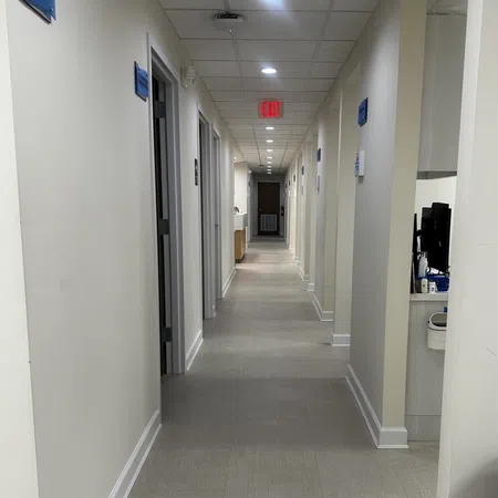 Long clean hallway in a modern office or clinic with multiple doors and overhead recessed lighting.