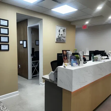 Modern medical office reception area with marble counter, certificates on wall, and open doorway to exam room.