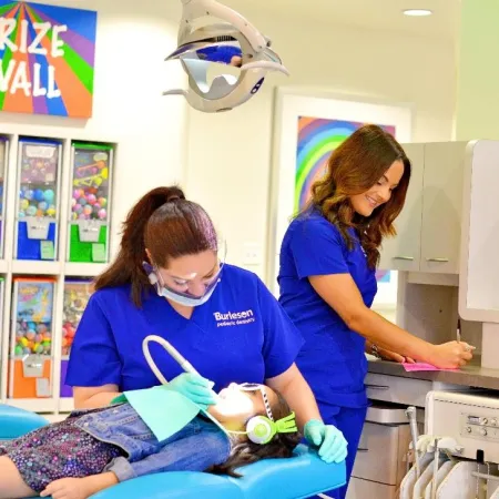 Pediatric dentist treating a child wearing headphones with a colorful prize wall in the background