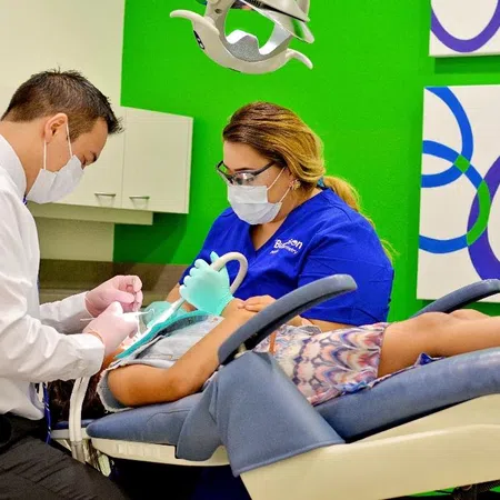 Dentist and assistant wearing masks treating a patient lying on a dental chair in a modern clinic.