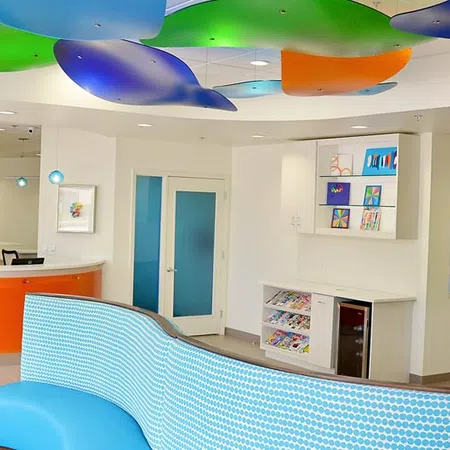 Modern office lobby with curved blue seating, colorful ceiling panels, and bright artwork on white walls.