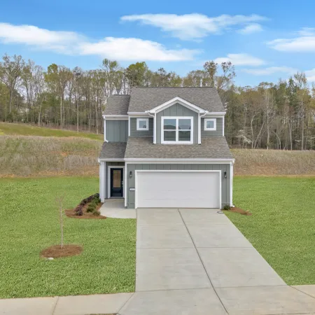Modern two-story house with gray siding and a driveway, surrounded by green lawn and trees.