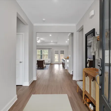 Modern home entryway with wooden flooring, white walls, and open view into living and kitchen areas with natural light.