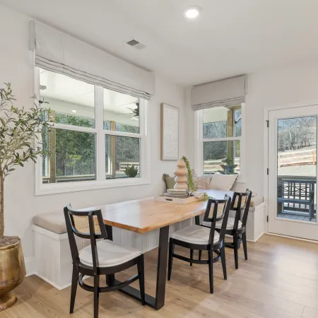 Bright dining nook with wooden table, black chairs, window seating, and potted plant in modern home