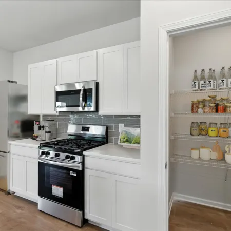 Modern kitchen with stainless steel appliances, white cabinets, gray backsplash, and pantry with organized shelves.