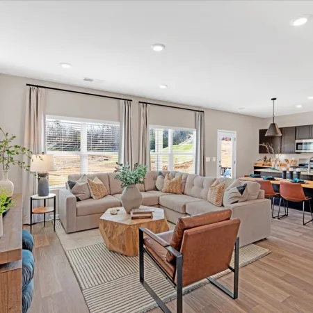 Modern living room with beige sectional sofa, wood accents, and large windows overlooking green yard.