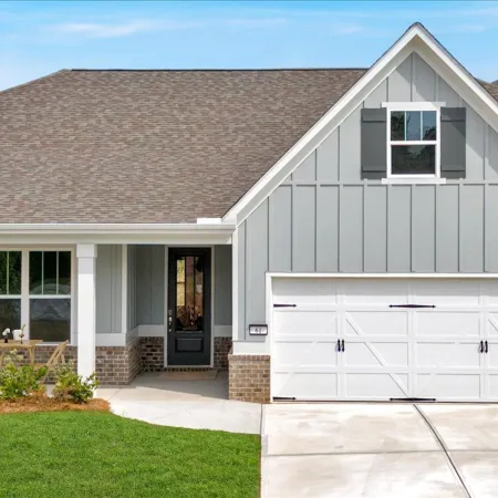 Modern single-story gray house with white garage door, front porch, and green lawn under blue sky