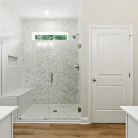 Modern bathroom with glass shower enclosure, chevron tile wall, wooden floor, and white doors and countertops
