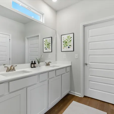 Modern white bathroom with double sink, large mirror, wooden floor, plants artwork, and sleek fixtures.