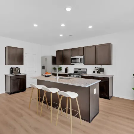 Modern kitchen with dark wood cabinets, granite island, white bar stools, stainless appliances, and light hardwood floors