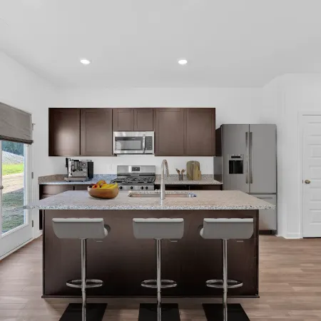 Modern kitchen with dark cabinets, granite countertops, and sleek bar stools overlooking a bright window view.