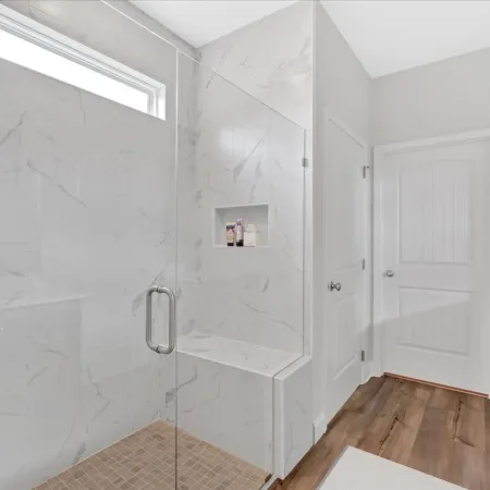Modern bathroom with glass shower, marble walls, wooden floor, and minimalist design for a serene ambiance.