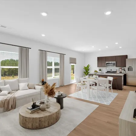 Bright open-concept living room and kitchen with white furniture, wooden floors, and large windows showcasing outdoor greenery.