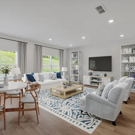 Bright modern living room with white furniture, blue patterned rug, wooden dining set, and large windows with curtains.