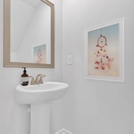 Modern bathroom with a white sink, mirror, and framed dreamcatcher artwork on light-colored walls.