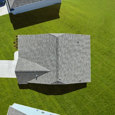 Aerial view of a grey-roofed house with a concrete driveway and green lawn on a residential street.