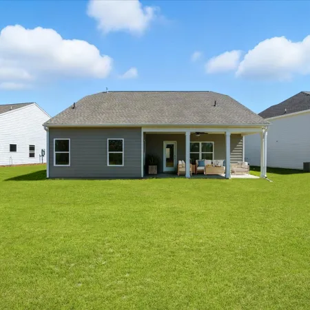 Modern single-story gray house with covered patio and large green backyard under blue sky.