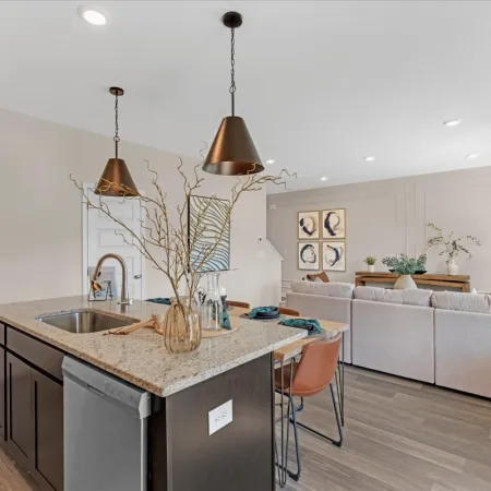 Modern kitchen with pendant lights and a cozy living area in the background, featuring stylish decor.