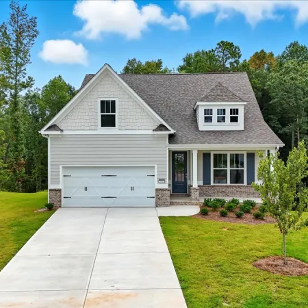 Modern two-story house with a gray roof, white facade, spacious driveway, and lush green lawn under a blue sky.