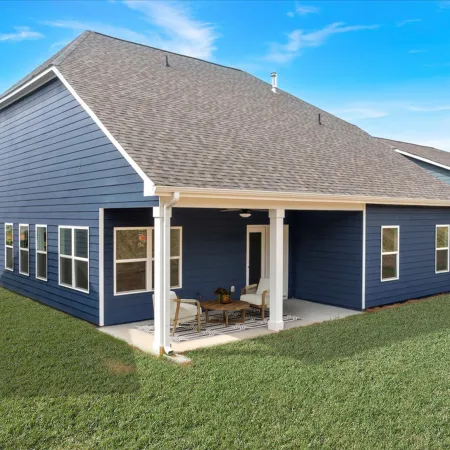Modern blue house with white trim features a covered patio with outdoor seating overlooking green lawn under blue sky.