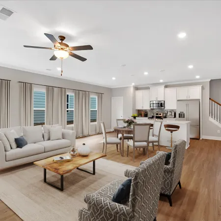 Bright open-concept living room with beige sofa, patterned armchairs, wood coffee table, dining set, and modern kitchen.