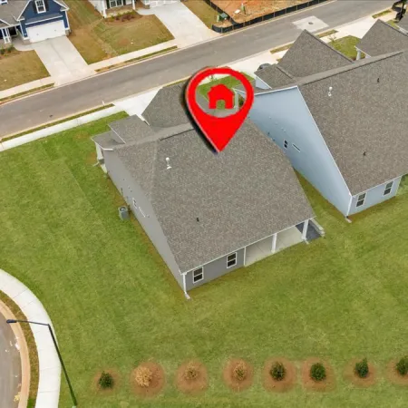 Aerial view of residential homes showing green lawns and street, with a location marker.