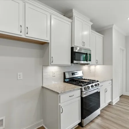 Modern kitchen with white cabinets, granite countertops, stainless steel gas stove and microwave, and light wood flooring.