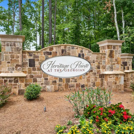 Stone entrance sign for Heritage Pointe at The Georgian surrounded by flowers and trees in a landscaped area.