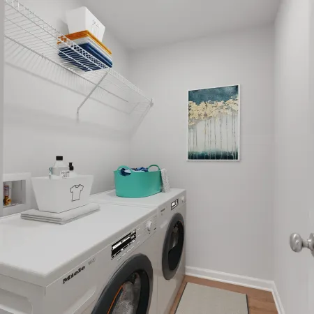 Compact laundry room with front-loading washer and dryer, white shelves, storage bins, and wall art.