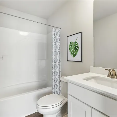 Modern white bathroom with bathtub, patterned shower curtain, toilet, white vanity, and framed leaf artwork.