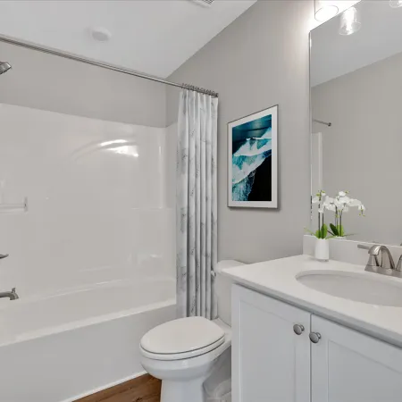 Modern clean bathroom with white bathtub, toilet, vanity with sink, mirror, and ocean wall art.