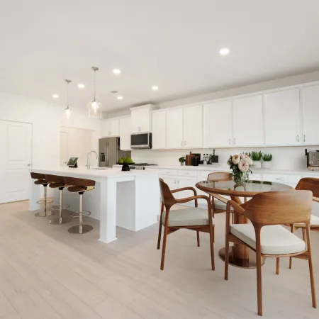 Bright modern kitchen with white cabinetry, island with bar stools, and wooden dining table with chairs.