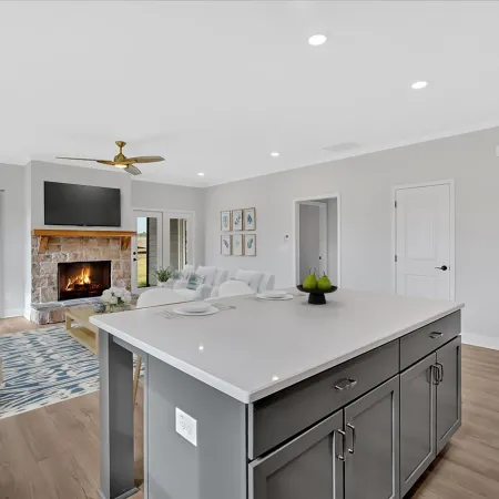 Bright modern living space with kitchen island, stone fireplace, large windows, and cozy seating area.