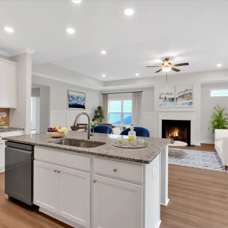 Modern open kitchen and living room with white cabinets, granite island, hardwood floors, and cozy fireplace.