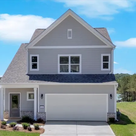Modern two-story gray house with a double garage, lawn, pond with fountain, and clear blue sky.